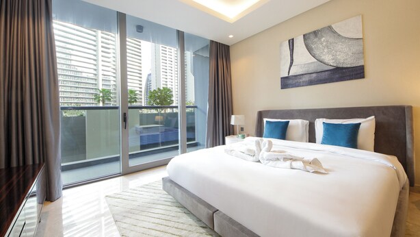 A modern hotel room with a large bed, a view of tall buildings, and a sliding glass door to the balcony. - Luxury 1BR at Sterling East Burj Views (Dubai)