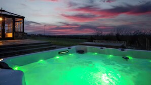 Una vasca idromassaggio con illuminazione verde, un ponte in legno e una struttura in vetro con luci.