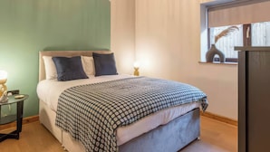 A bedroom with a bed, bedside tables, a window with a view, and a wooden ceiling. - Swan Cottage (Gaerwen)