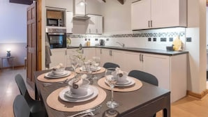A modern kitchen with white cabinets, a central island, and a dining area set for six with a dark table and beige placemats. - Swan Cottage (Gaerwen)