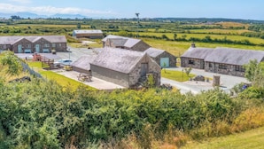 A rural setting with stone buildings, a paved road, and open fields. - Swan Cottage (Gaerwen)
