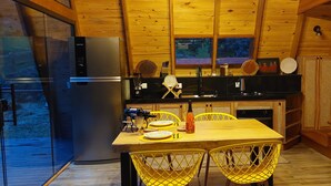 A compact kitchen with wooden walls, a dining table with yellow chairs, a refrigerator, and a stove. - Exclusive A-Frame chalet with private pool. (Itajubá)