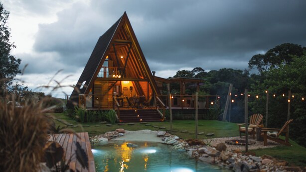 A wooden cabin with a triangular roof, a swimming pool, and a deck area with chairs. - Exclusive A-Frame chalet with private pool. (Itajubá)