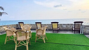 Outdoor wicker chairs and a bench on artificial grass by a stone wall with a view of the ocean. - Cinnamon Tree Resort Akurala-Hikkaduwa (Madampagama)