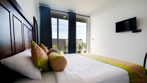 A hotel room with a large bed, a flat-screen TV mounted on the wall, and a view of the outdoors through a sliding glass door. - Cinnamon Tree Resort Akurala-Hikkaduwa (Madampagama)