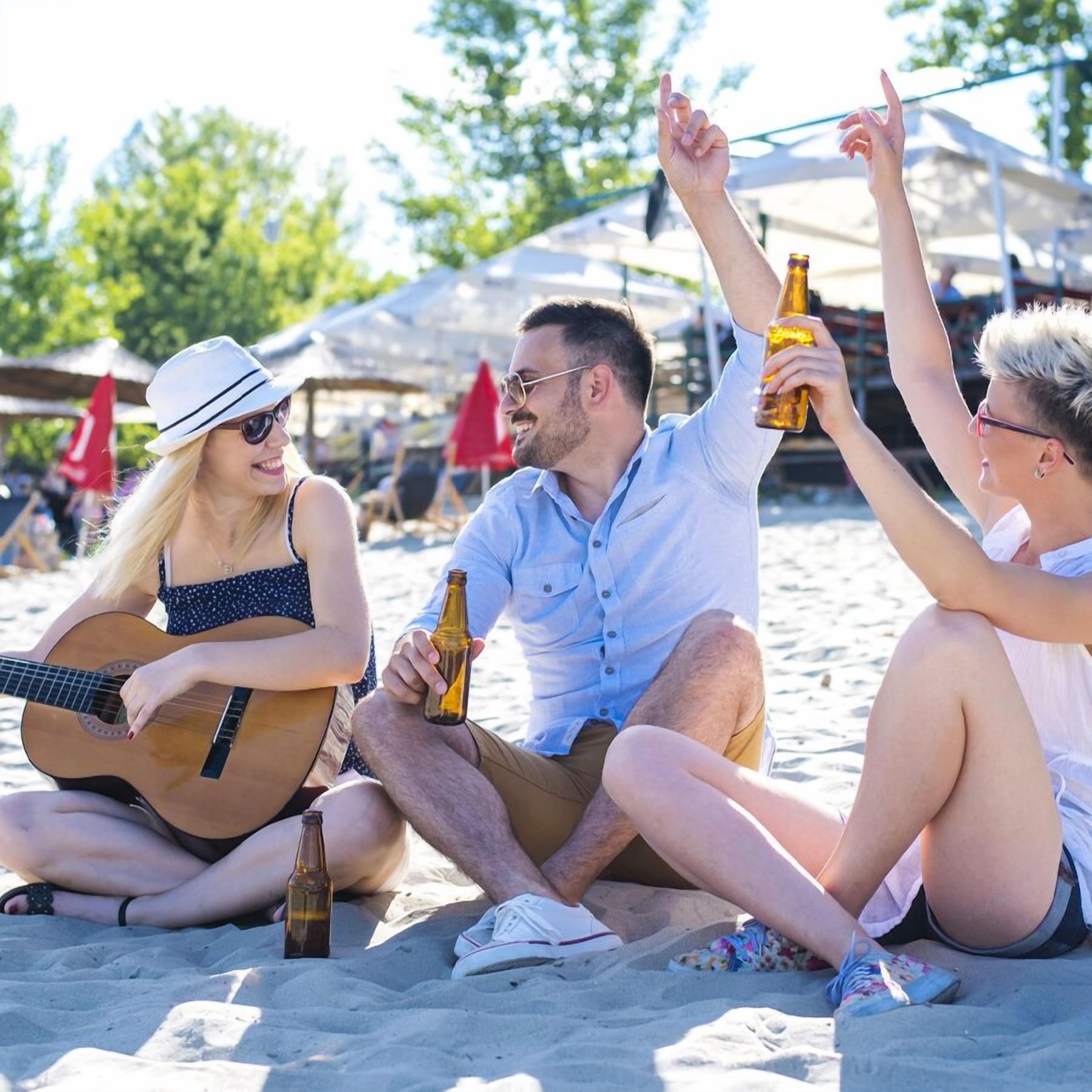 A group of people sitting on a sandy beach, with one person playing a guitar.