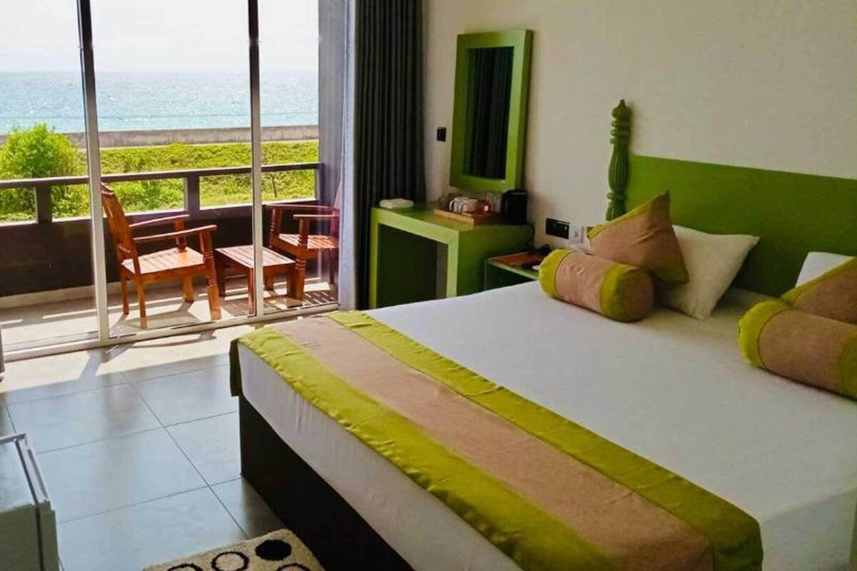 A hotel room with a large bed, a green nightstand, a chair, and a view of the ocean through a sliding door.