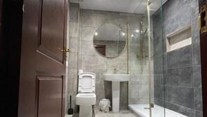 Un baño moderno con inodoro, lavamanos y ducha con mampara de vidrio.
