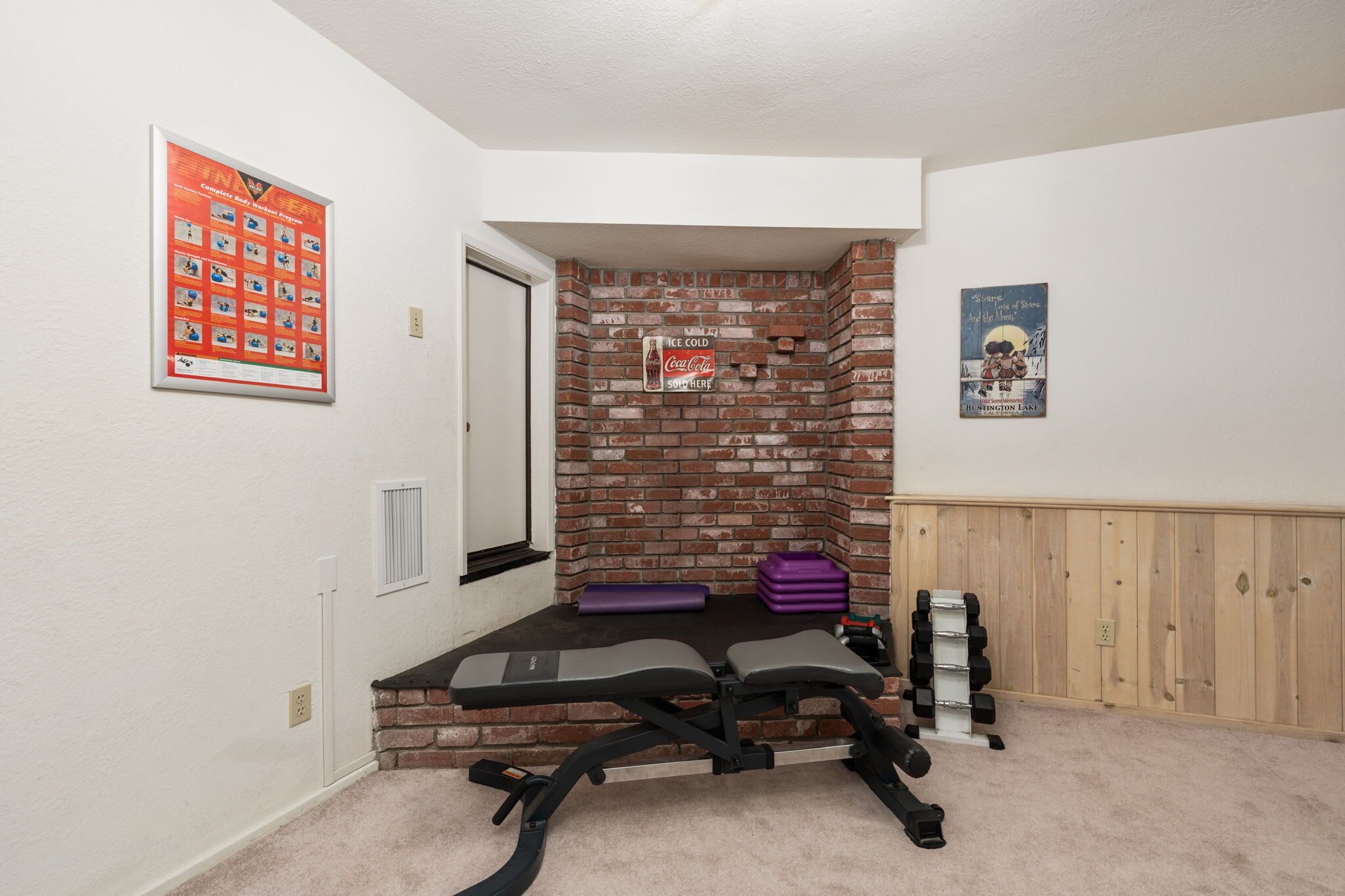 A home gym with a bench press, dumbbells, and a brick wall.