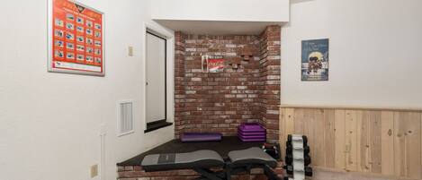 A home gym with a bench press, dumbbells, and a brick wall.
