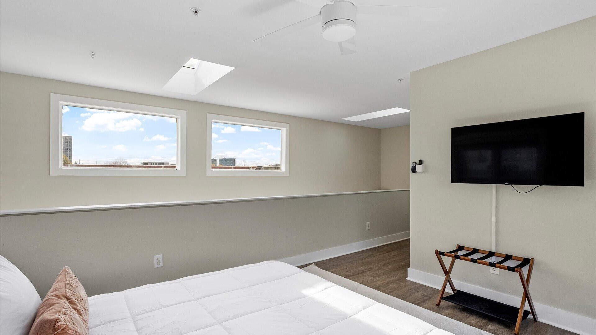 A bedroom with a bed, two windows, a ceiling fan, a flat-screen TV, and a small table.