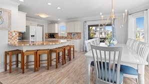 Una cocina moderna con armarios blancos, una isla grande con taburetes y un comedor con mesa y sillas blancas.