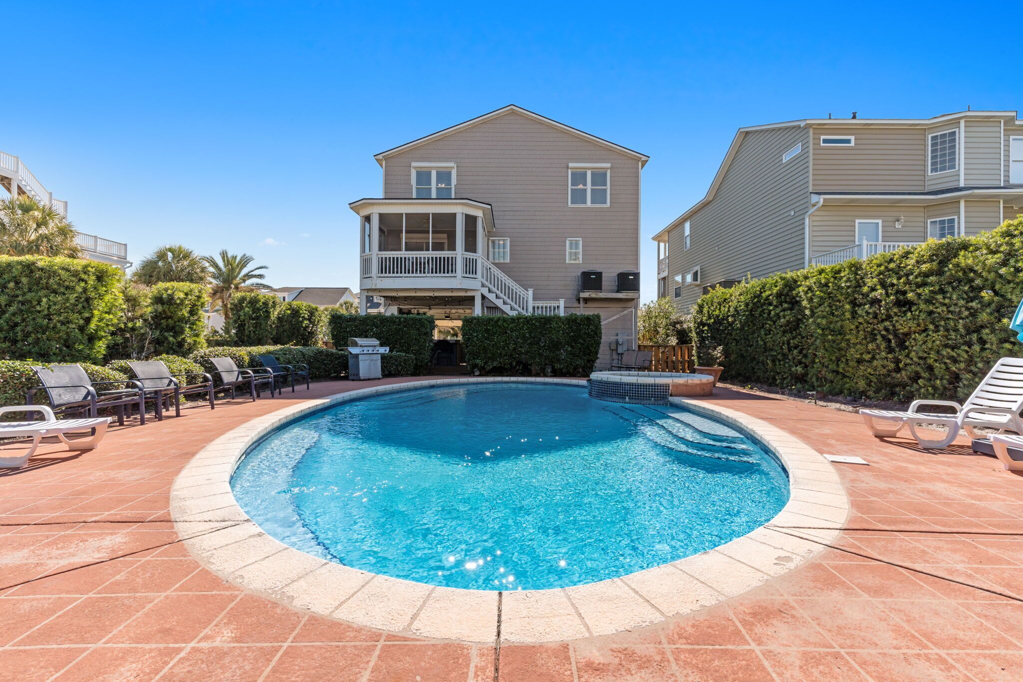 Une piscine avec des chaises longues, une terrasse couverte et une maison à deux étages en arrière-plan.