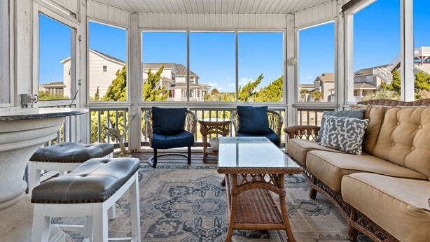 Un patio techado con muebles de mimbre, una mesa de vidrio y un sofá color beige.