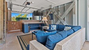 Un espacio exterior acogedor con un sofá azul, mobiliario de mimbre y una zona de bar con una televisión.