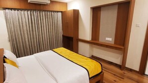 A hotel room with a bed, a wardrobe, a desk, and a window with curtains. - KRISHNA SAI SUITES (Rahata)