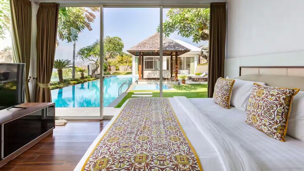 A bedroom with a large bed, a TV, and a view of a swimming pool and outdoor area.