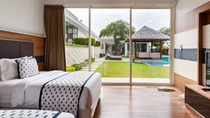 A modern hotel room with a large bed, a TV, and a sliding glass door leading to a pool area.