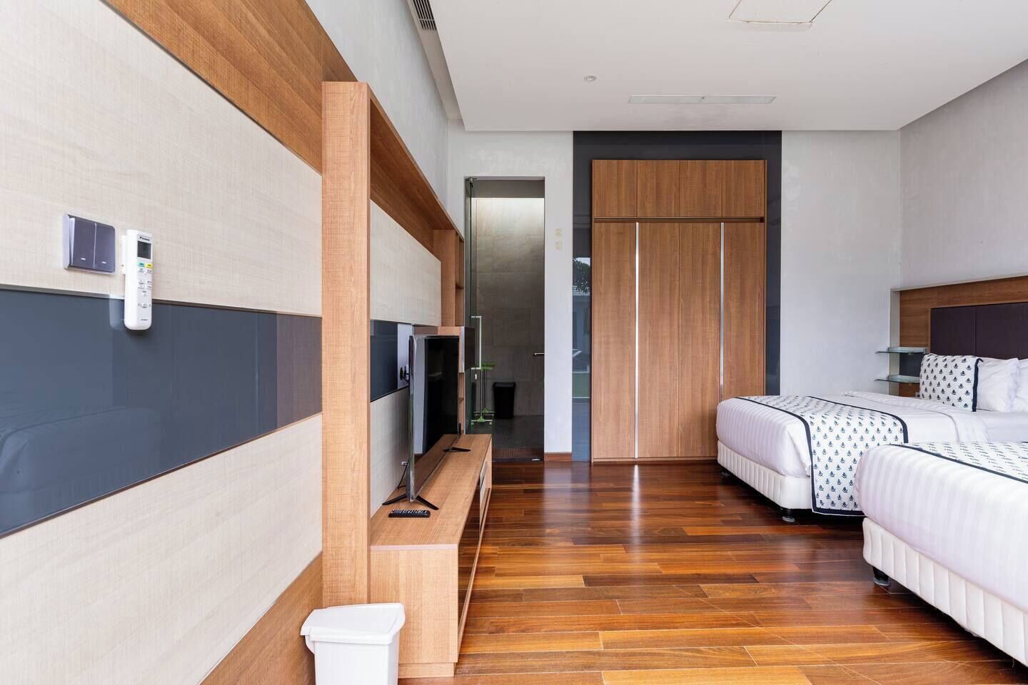 Ein modernes Hotelzimmer mit Holzboden, einem Bett mit gemusterten Bettbezügen, einem Fernseher auf einem Holzschrank und einem Kleiderschrank mit Spiegel.