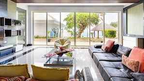 A modern living room with a glass coffee table, leather sofa, and a large sliding glass door leading to a balcony with a view of the sea.