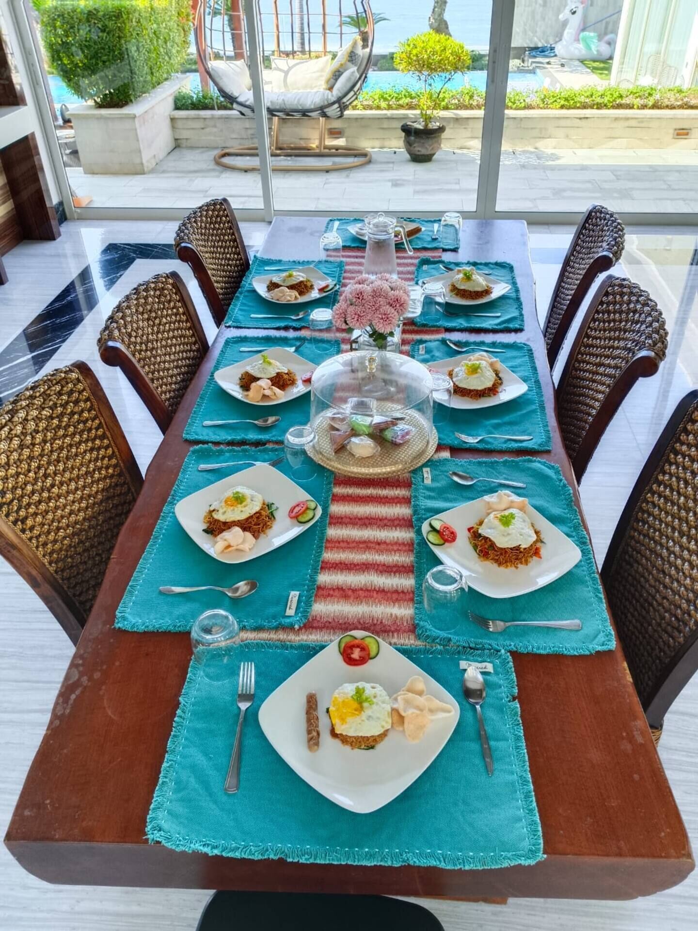 Una mesa de comedor dispuesta con platos de comida, un jarrón de flores y un camino de mesa a rayas.