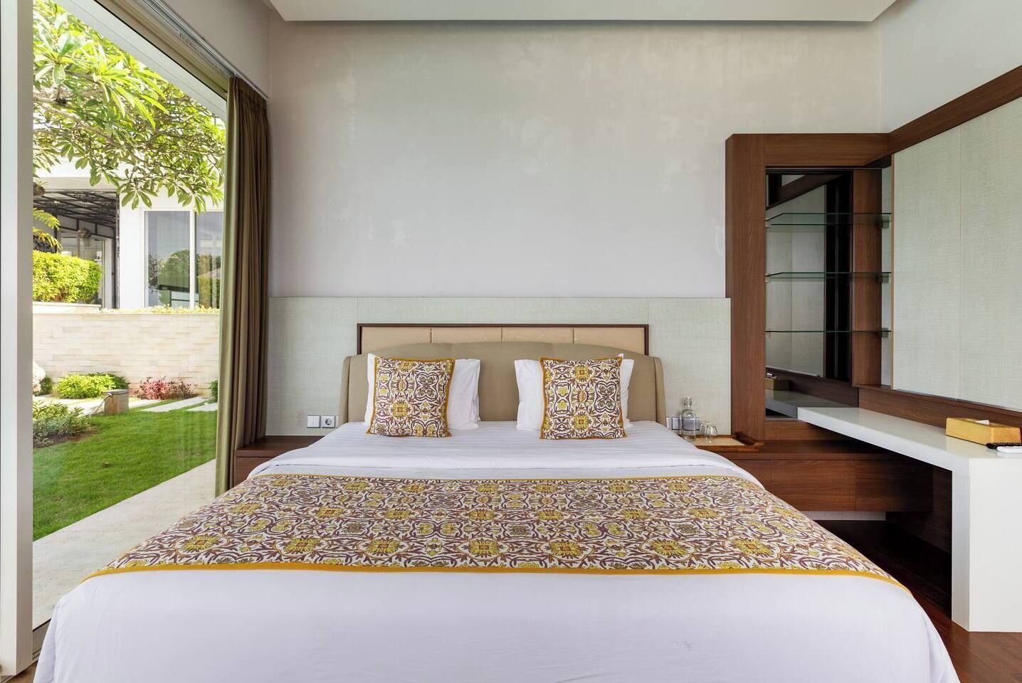 Una habitación de hotel moderna con una cama grande, un escritorio integrado y un amplio ventanal con vistas al jardín.