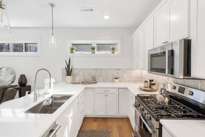 A modern kitchen with white cabinetry, stainless steel appliances, and a window with plants. - G St Loft, Downtown Bentonville (Bentonville)