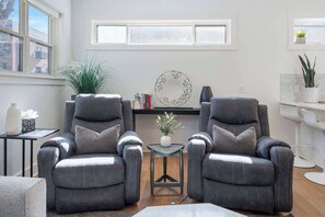 A modern living room with two grey armchairs, a small side table with a plant, a round wall decoration, and a white shelf with plants. - G St Loft, Downtown Bentonville (Bentonville)