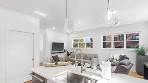 A modern kitchen with a built-in sink, a dining area with a sofa and chairs, and a large window with a view of a brick building. - G St Loft, Downtown Bentonville (Bentonville)