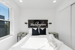 A modern bedroom with a large bed, a headboard with a motivational quote, two bedside tables, and a window providing a view of the outside. - G St Loft, Downtown Bentonville (Bentonville)