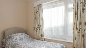 Une chambre avec un lit simple, une fenêtre ornée de rideaux à motifs floraux et un mur uni.