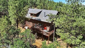 A cabin with a deck, surrounded by dense forest. - Minnie Mine Cabin Retreat 4 Bedroom Cabin (Prescott)