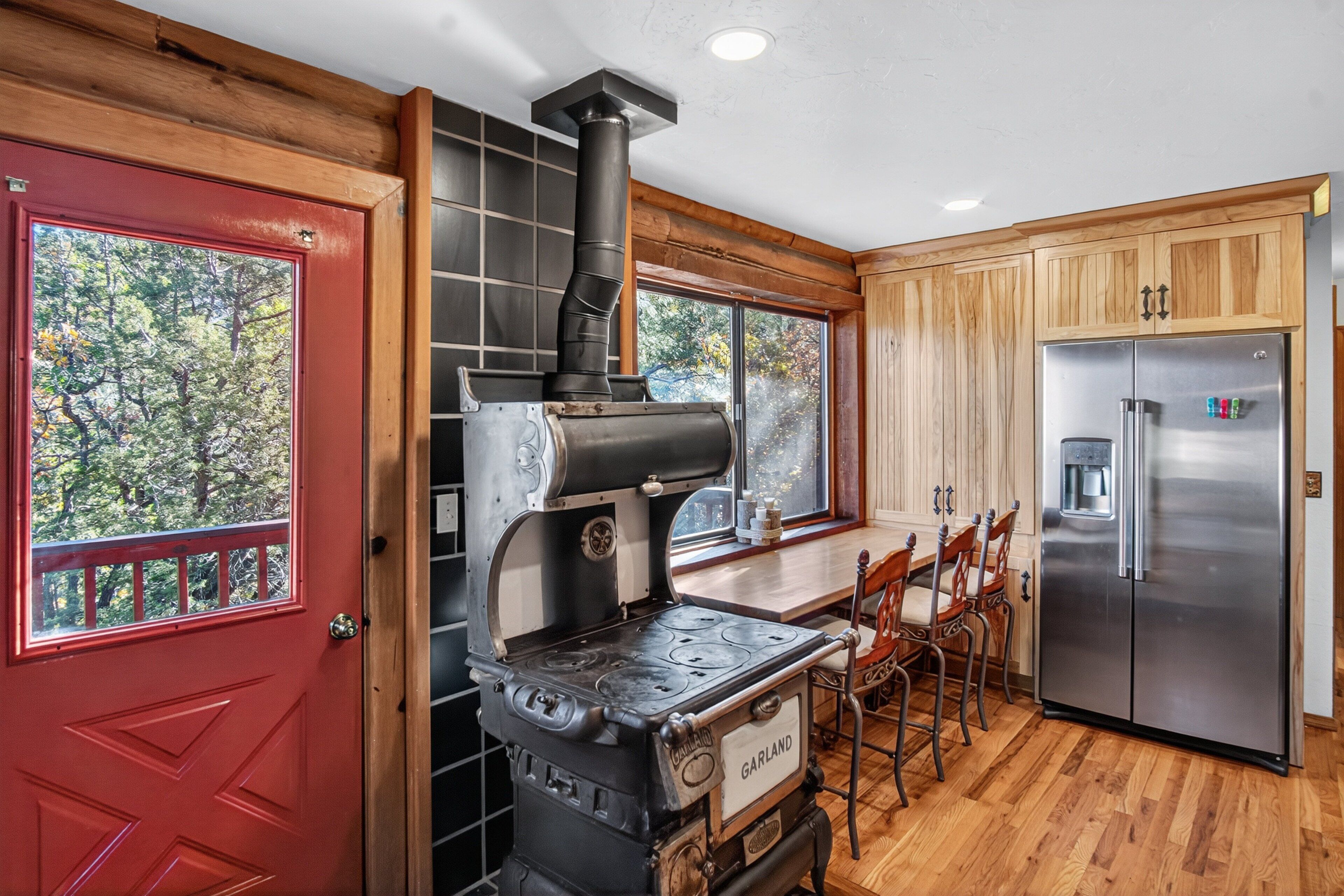 A kitchen with a vintage stove, wooden cabinets, a stainless steel refrigerator, and a red door.