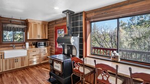 A cabin-style kitchen with wooden cabinets, a stove, and a dining area with a view of trees. - Minnie Mine Cabin Retreat 4 Bedroom Cabin (Prescott)