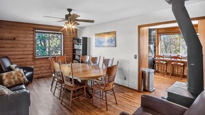 A cozy cabin interior with a wooden dining table, chairs, a ceiling fan, a fireplace, and a bookshelf. - Minnie Mine Cabin Retreat 4 Bedroom Cabin (Prescott)