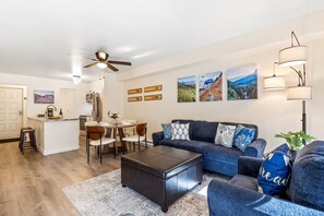 A modern living room with a dark sofa, a coffee table, and a dining area with chairs and a table. - Fall Line 107 2 Bedroom Condo (Telluride)