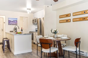 A modern kitchen with a central island, white cabinetry, stainless steel appliances, and a dining area with wooden chairs and a round table. - Fall Line 107 2 Bedroom Condo (Telluride)
