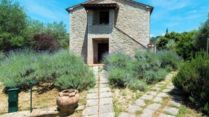 A stone building with a central doorway and a small window, surrounded by a stone pathway and greenery. - Farmhouse Il Mulino delle canutole - Il Granaio (Magione)