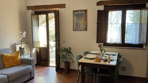 A dining area with a table set for two, a sofa with a yellow pillow, a potted plant, and a wall-mounted picture. - Farmhouse Il Mulino delle canutole - Il Granaio (Magione)