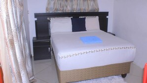 A neatly made bed with a blue note, a dark headboard, and a decorative pillow. - Blue Ridge Escape Guest House (Kasane)