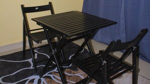 A room with a black metal table and chairs, a colorful abstract painting on the wall, and a blue curtain. - Blue Ridge Escape Guest House (Kasane)