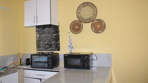 A kitchen with white cabinets, a black microwave, a toaster, and decorative plates on the wall. - Blue Ridge Escape Guest House (Kasane)