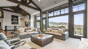 A spacious living room with large windows, a sectional sofa, and a marble coffee table. - Abode on Ruby Run, ski-in/ski-out, hot tub, sauna, fire pit (Park City)