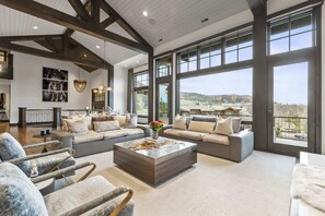 A spacious living room with large windows, a sectional sofa, and a marble coffee table. - Abode on Ruby Run, ski-in/ski-out, hot tub, sauna, fire pit (Park City)
