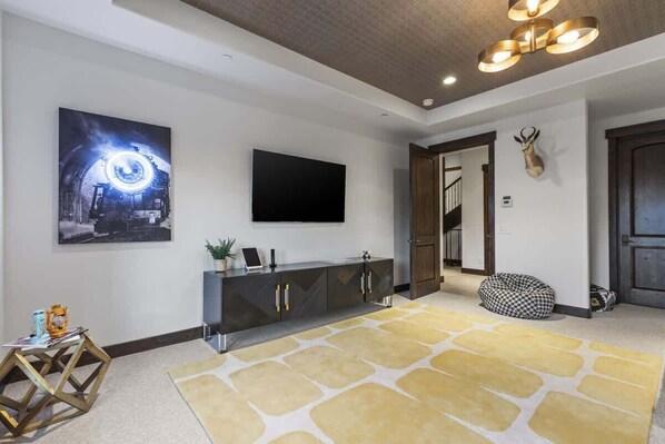 A modern living room with a large flat-screen TV, a decorative wall piece, a patterned rug, and a wooden cabinet. - Abode on Ruby Run, ski-in/ski-out, hot tub, sauna, fire pit (Park City)