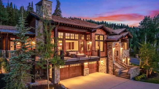 A large, multi-story log cabin with a stone chimney, large windows, and a stone staircase leading to the entrance. - Abode on Ruby Run, ski-in/ski-out, hot tub, sauna, fire pit (Park City)