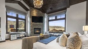 A bedroom with a fireplace, large windows, a bed, and a desk area. - Abode on Ruby Run, ski-in/ski-out, hot tub, sauna, fire pit (Park City)