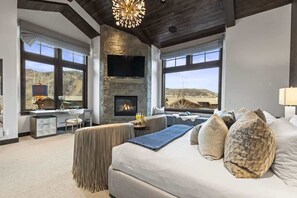 A bedroom with a fireplace, large windows, a bed, and a desk area. - Abode on Ruby Run, ski-in/ski-out, hot tub, sauna, fire pit (Park City)