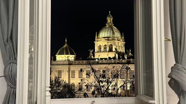Blick auf ein historisches Gebäude mit einer großen Kuppel und Statuen, sichtbar durch ein Fenster mit Vorhängen.