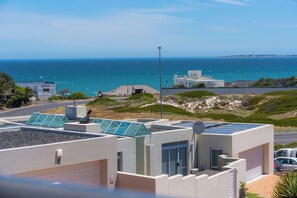 A modern building with solar panels, a garage, and a view of the ocean. - Luxury Family Villa - Ocean & Mountain Views (Bloubergstrand,)